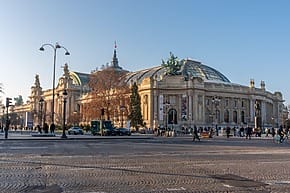 Exterior view of the Grand Palais with glass dome, bustling street, pedestrians, and light traffic on a clear day.