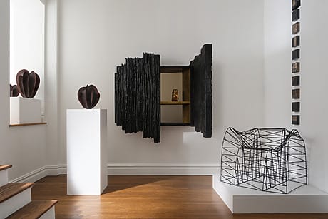 Modern art gallery featuring abstract sculptures and geometric installations in a minimalistic white room with wooden flooring.