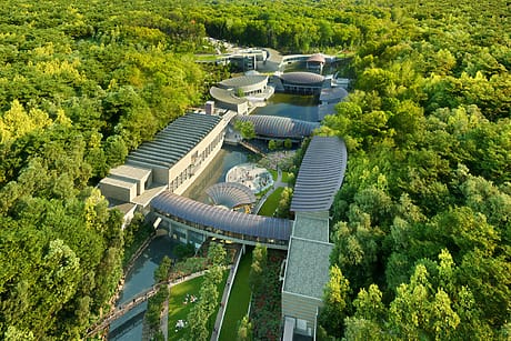 Aerial view of a modern architecture building complex surrounded by lush green forest and winding pathways.