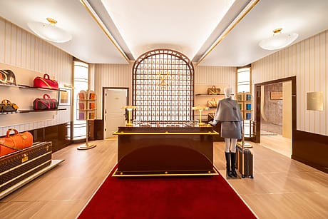 Luxury boutique store interior with designer bags on shelves, mannequin, suitcase, and elegant decor.