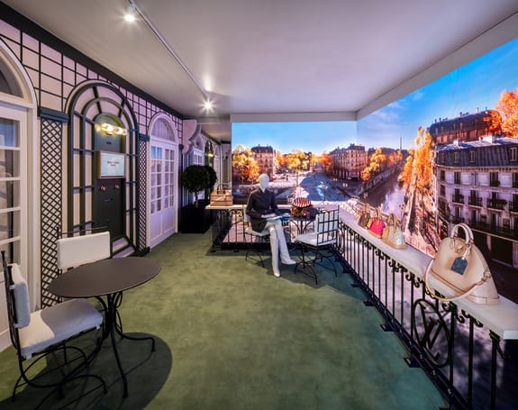 Luxury showroom with elegant furniture and a large scenic backdrop of Paris in autumn, featuring vibrant fall foliage.