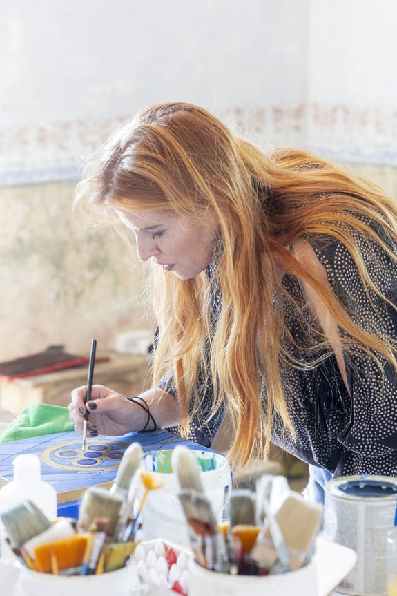 Person with long hair painting a colorful canvas with brushes in the foreground