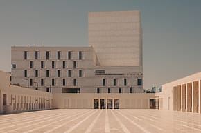 Modern architectural building with geometric design and large open courtyard under a clear blue sky.