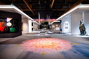 Art gallery interior with vibrant paintings, modern sculptures, and a large flower design on the floor.