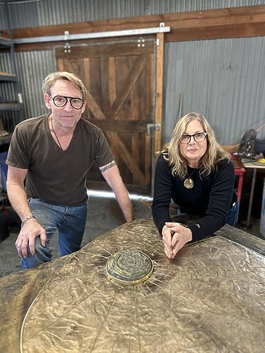Two adults in a workshop standing by a table with a circular metallic object.