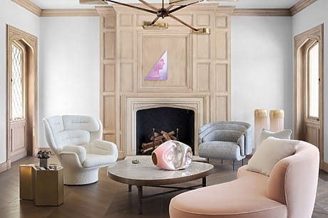 Modern living room with pastel furniture, geometric chandelier, and wooden fireplace.