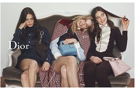 Three models sitting on a sofa, showcasing Dior fashion with handbags and elegant outfits.