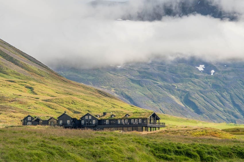 Wooden lodge surrounded by lush green mountains and misty clouds in a remote landscape.