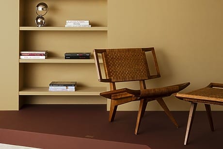Modern room with wooden chair and matching table, built-in wall shelf displaying books and decorative items against a beige wall.