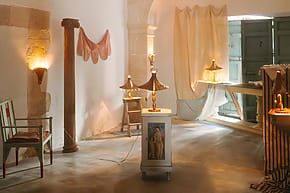 Warmly lit room with classical decor, including sculptures, draped fabrics, and a column, creating an inviting atmosphere.