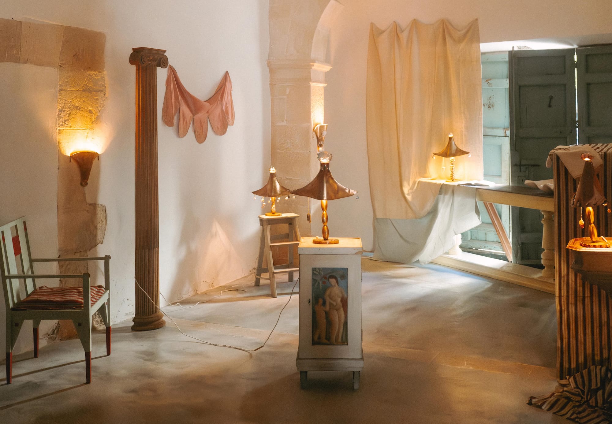 Warmly lit room with classical decor, including sculptures, draped fabrics, and a column, creating an inviting atmosphere.