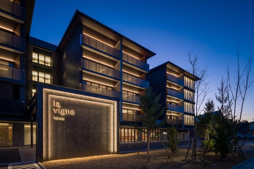 Modern building at dusk with illuminated sign reading "la vigne" and trees in the foreground.