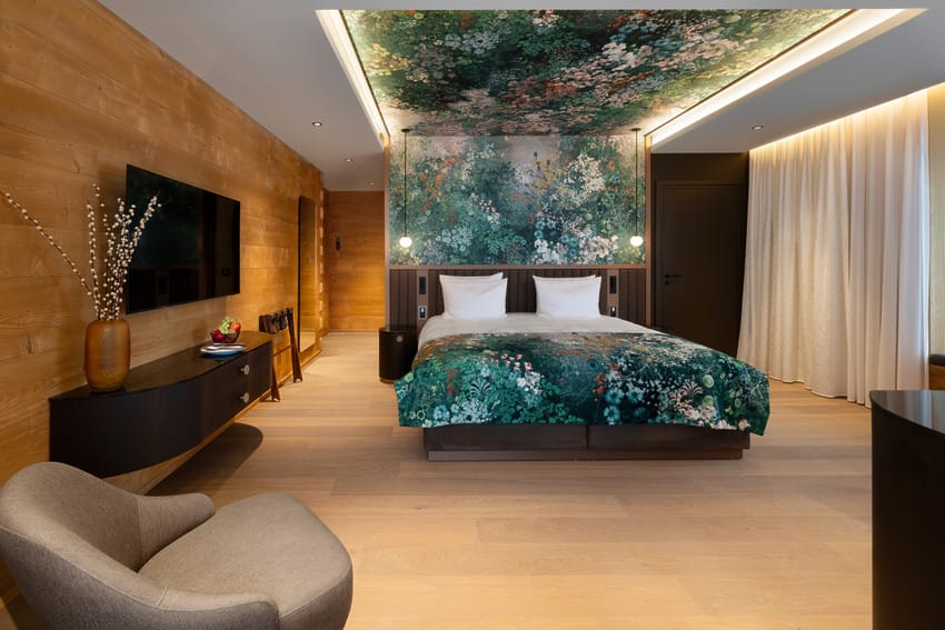 Modern hotel room with a vibrant floral ceiling mural, wooden walls, and a large bed with matching floral bedding.
