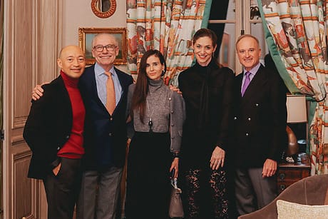 Five people smiling and posing indoors with elegant attire and colorful curtains in the background.