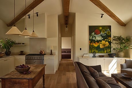 Cozy kitchen with wooden beams, rustic table, modern appliances, and a vibrant floral painting on the wall.