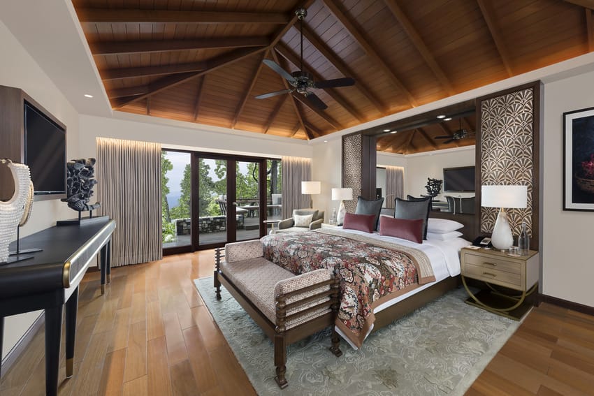 Luxurious bedroom with wooden ceiling, large bed, elegant decor, and a view of greenery through sliding glass doors