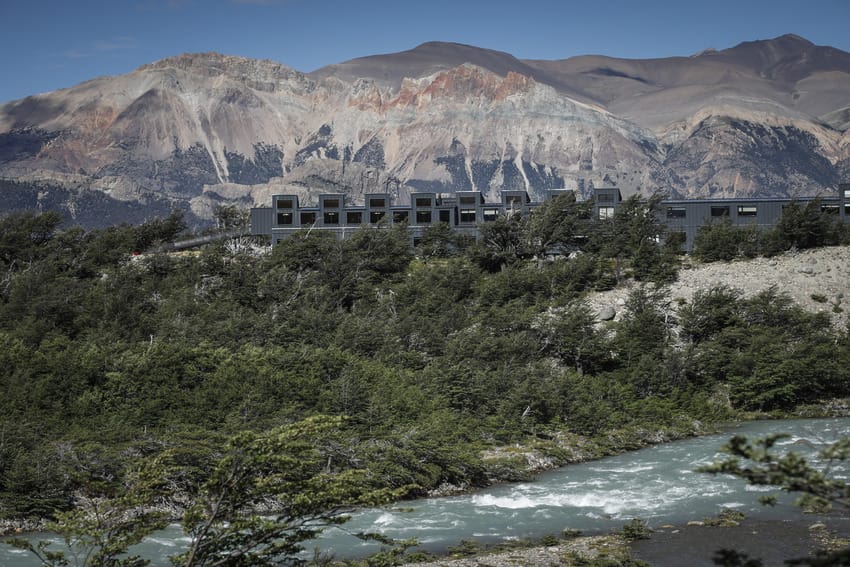 Modern building near a flowing river with mountainous landscape in the background under a clear blue sky.