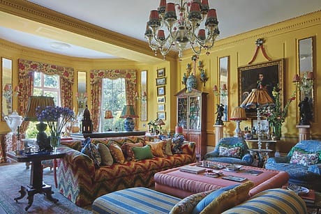 Colorful, eclectic living room with patterned furniture, chandelier, vibrant decor, and large windows providing natural light.