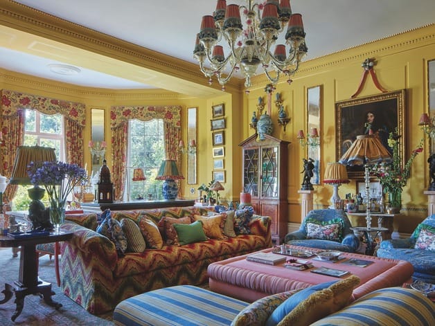 Colorful, eclectic living room with patterned furniture, chandelier, vibrant decor, and large windows providing natural light.