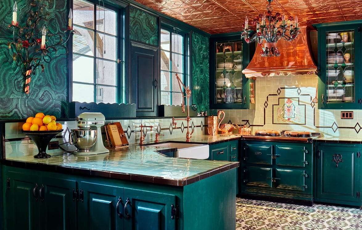 Eclectic kitchen with emerald cabinets, copper range hood, patterned floor tile, and a decorative chandelier.