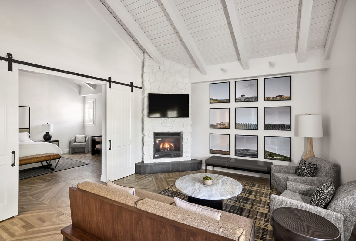 Modern living room with a fireplace, wall art, and sliding doors leading to a bedroom, featuring stylish furniture and decor.