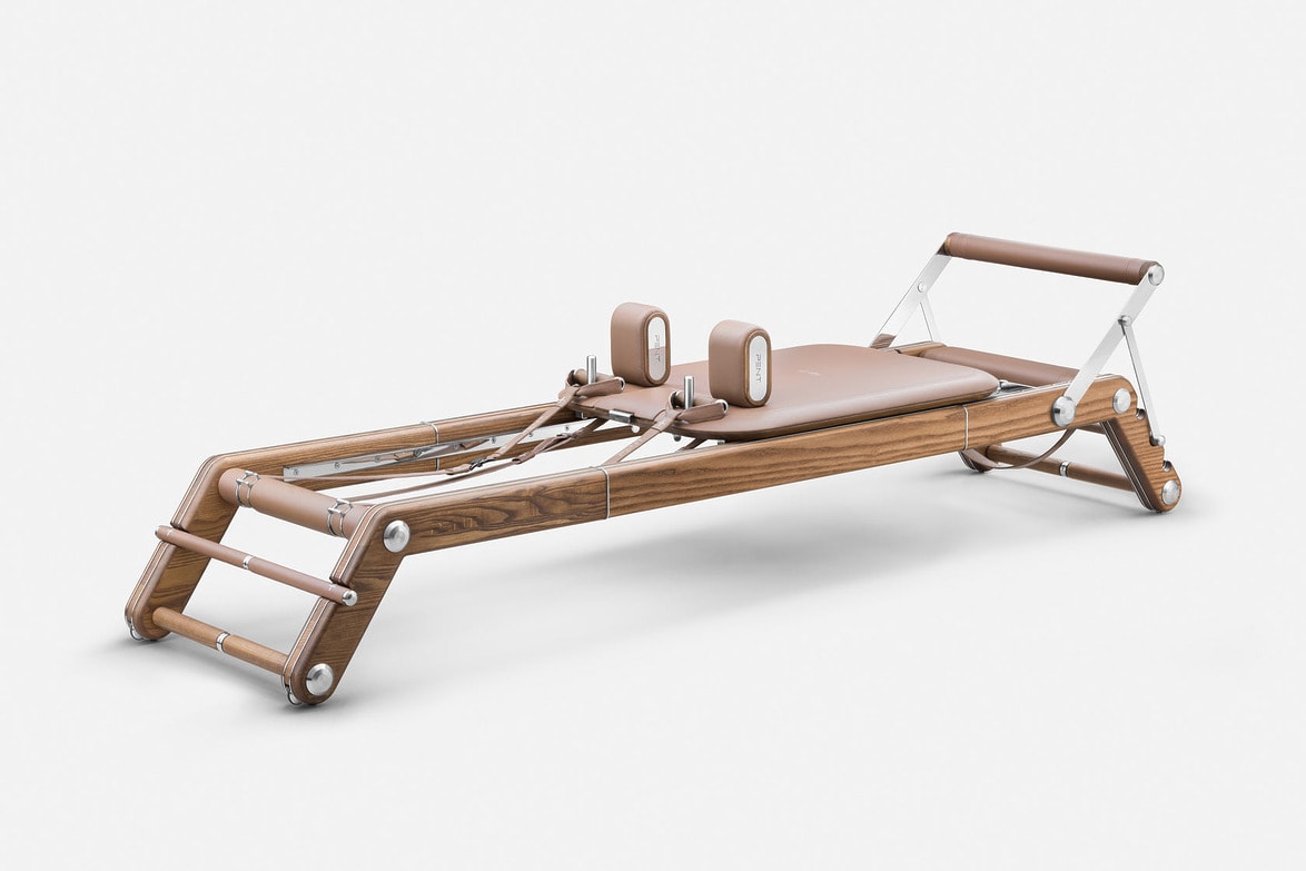 Wooden Pilates reformer with leather accents on a white background.