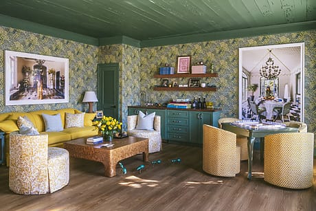 Eclectic living room with yellow sofa, patterned wallpaper, green cabinets, and colorful decorations.