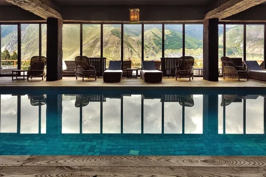 Indoor pool with lounge chairs and mountain views through large windows, creating a relaxing and scenic environment.