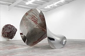 Abstract metallic and textured sculptures in a modern art gallery setting with high ceilings and bright lighting.