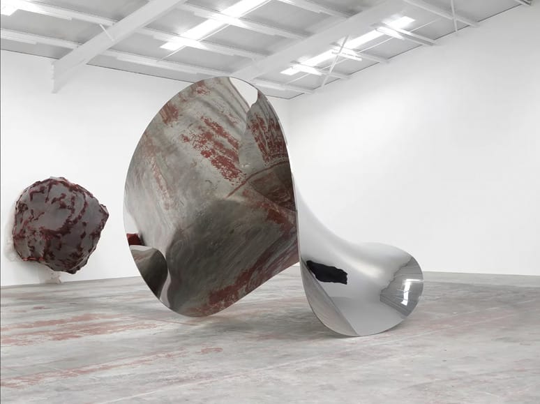 Abstract metallic and textured sculptures in a modern art gallery setting with high ceilings and bright lighting.