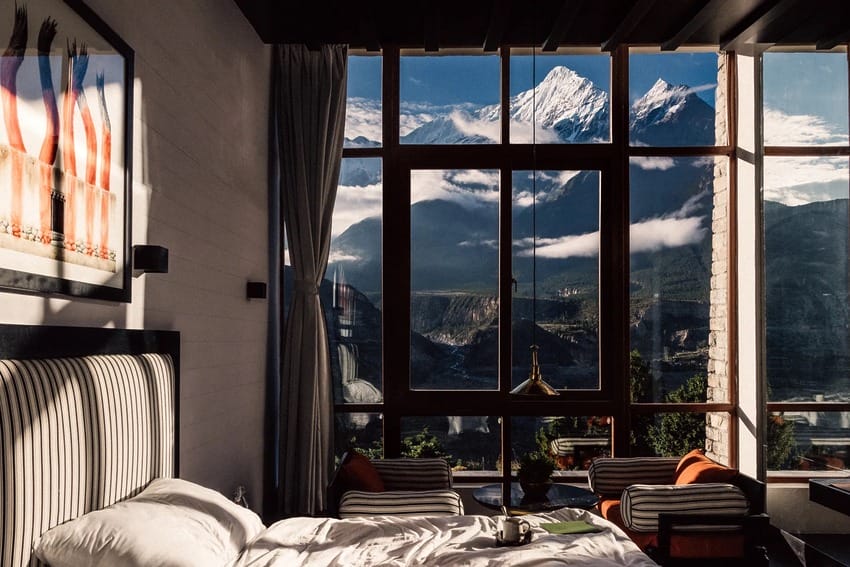 Luxurious bedroom with large windows offering a stunning view of snow-capped mountains and a clear blue sky.