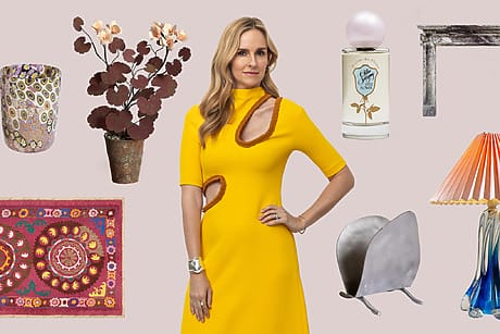 Person in yellow dress surrounded by home decor items, including a lamp, rug, vase, plants, and perfume bottle on a soft background.