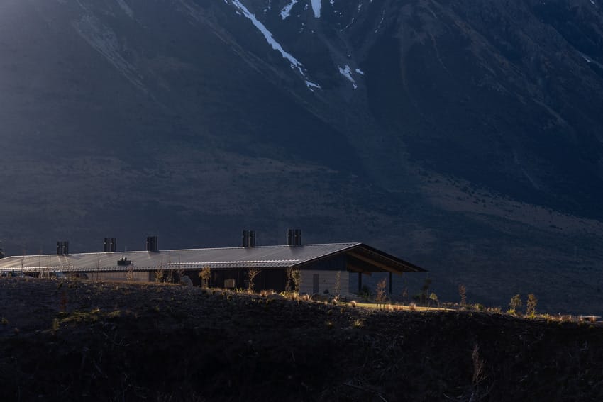 Modern building with metal roof set against a backdrop of misty mountains and forested terrain at dusk.