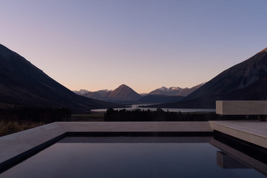 Infinity pool with mountain and lake view at dusk, featuring a serene landscape and clear sky in the background