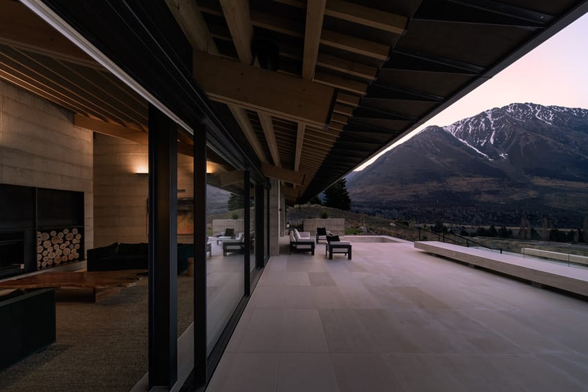 Mountain view at sunset from a modern open-plan house patio with large windows and outdoor seating.