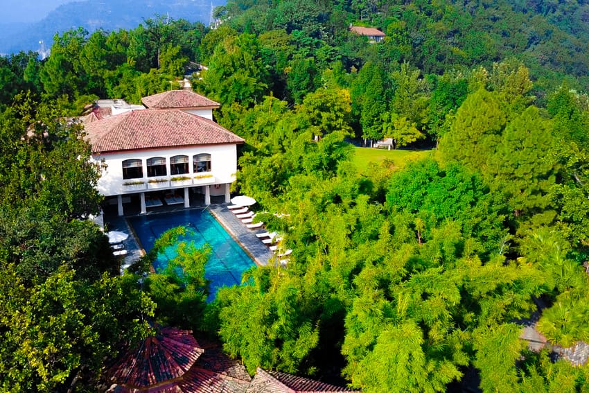 Aerial view of a luxury villa with a swimming pool surrounded by lush green forest.