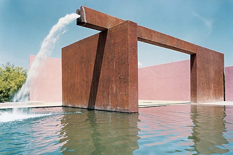 Modern architectural water feature with cascading water into a reflective pool, set against a clear blue sky.