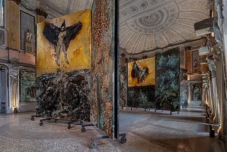 Art gallery with large abstract paintings on rolling panels in an ornate room with a detailed ceiling and arched doorways.