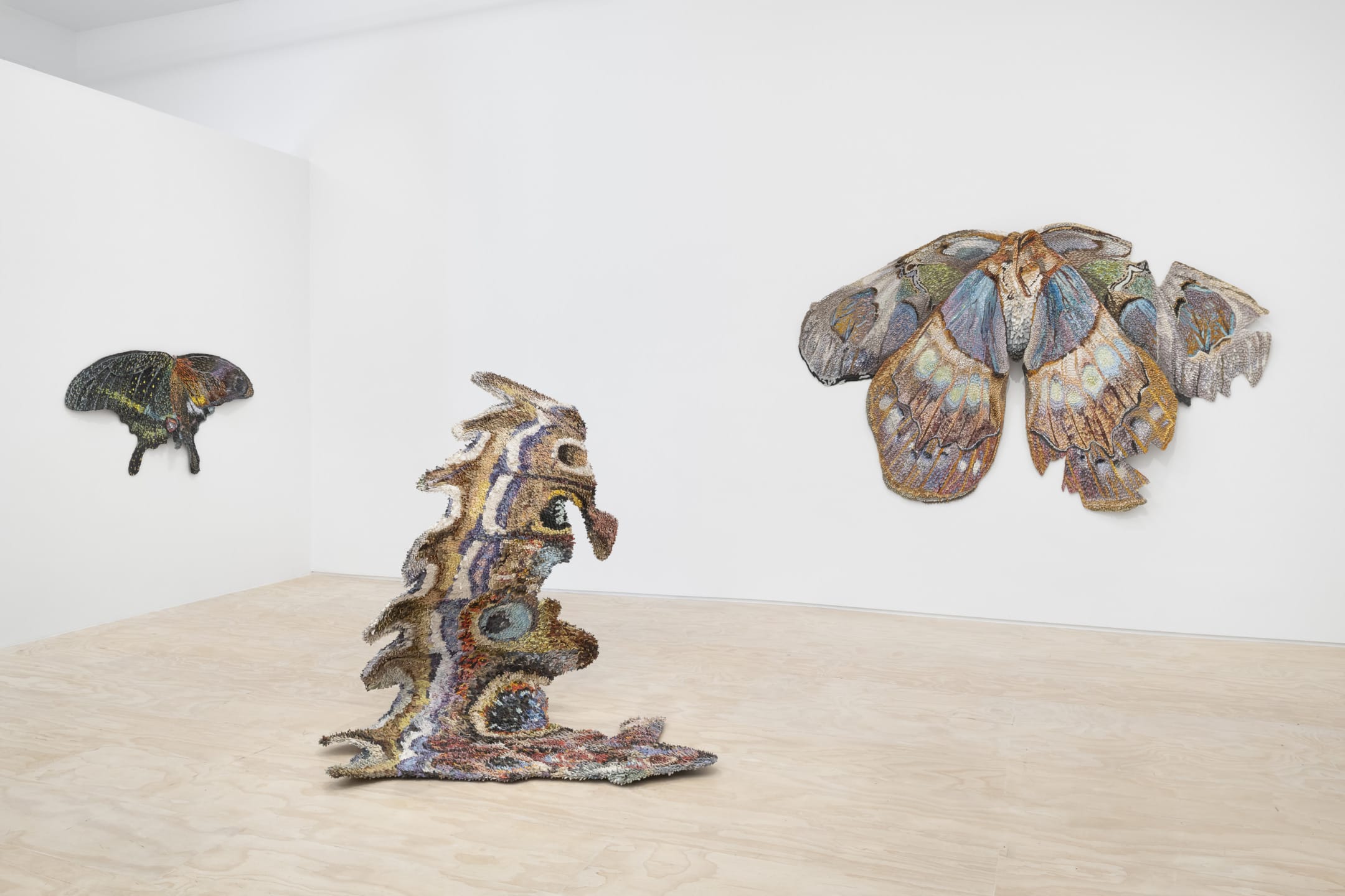Art installation with colorful, textured moth-like sculptures displayed on gallery walls and floor, emphasizing nature-inspired designs.