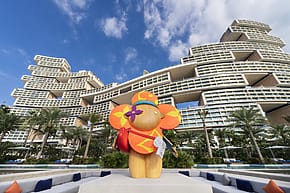 Colorful sculpture of an elephant with sunglasses in front of a unique, modern architectural building under a blue sky.