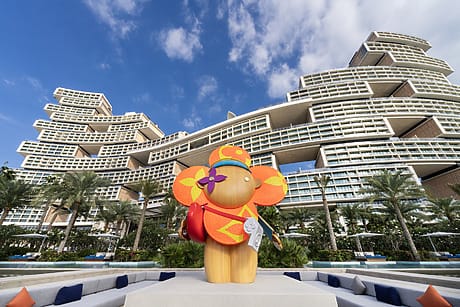 Colorful sculpture of an elephant with sunglasses in front of a unique, modern architectural building under a blue sky.