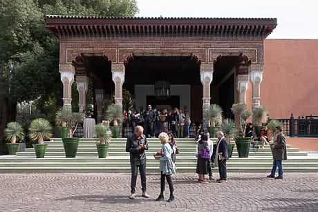 People gathered outside an ornate building with columns, talking and enjoying the courtyard setting.