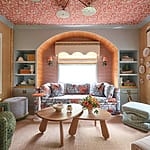 Colorful living room with patterned ceiling, floral sofa, wooden tables, and decorative shelves and walls.
