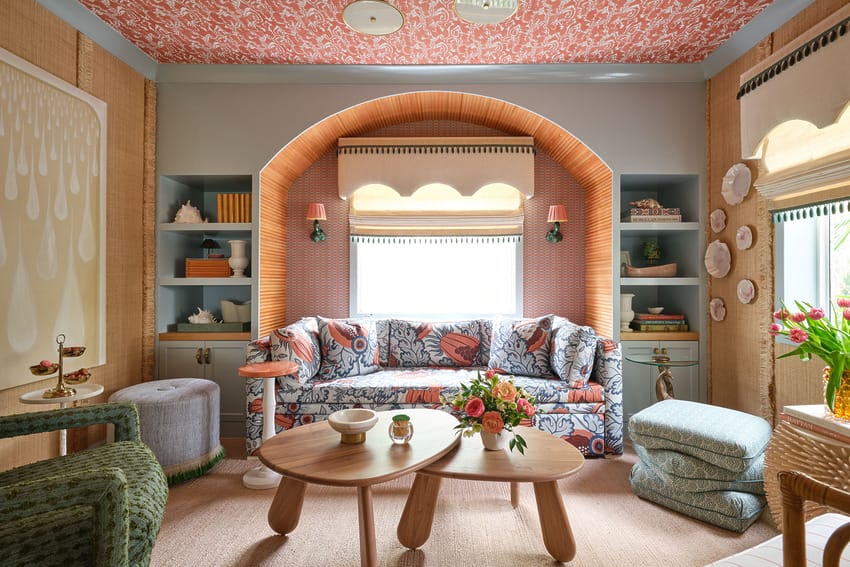Colorful living room with patterned ceiling, floral sofa, wooden tables, and decorative shelves and walls.
