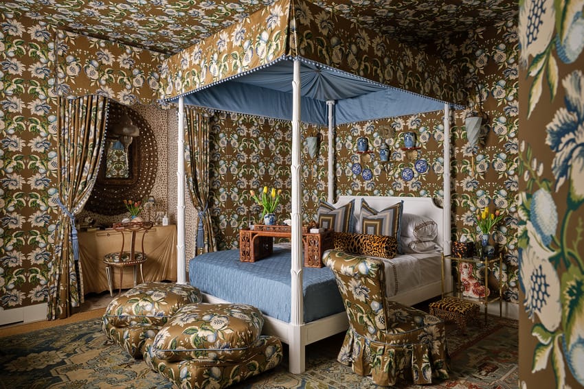 Ornate bedroom with floral wallpaper, canopy bed, patterned pillows, and matching drapes creating a cozy, vintage atmosphere.