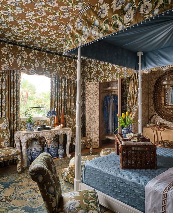 Luxurious bedroom with floral patterned wallpaper and drapes, a canopy bed, decorative vases, and a window view.