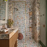 Colorful bathroom with geometric patterned tiles, wooden vanity, brass fixtures, and a clear glass shower door.