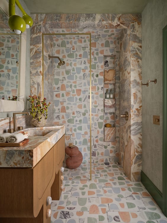 Colorful bathroom with geometric patterned tiles, wooden vanity, brass fixtures, and a clear glass shower door.