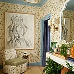 Elegant floral-themed room with abstract art, floral chair, mirror, chandelier, and flower arrangements on a mantel.