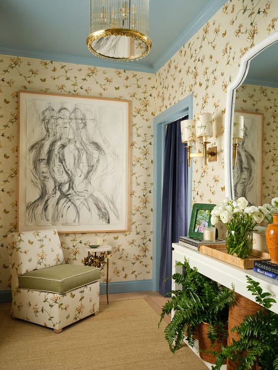Elegant floral-themed room with abstract art, floral chair, mirror, chandelier, and flower arrangements on a mantel.